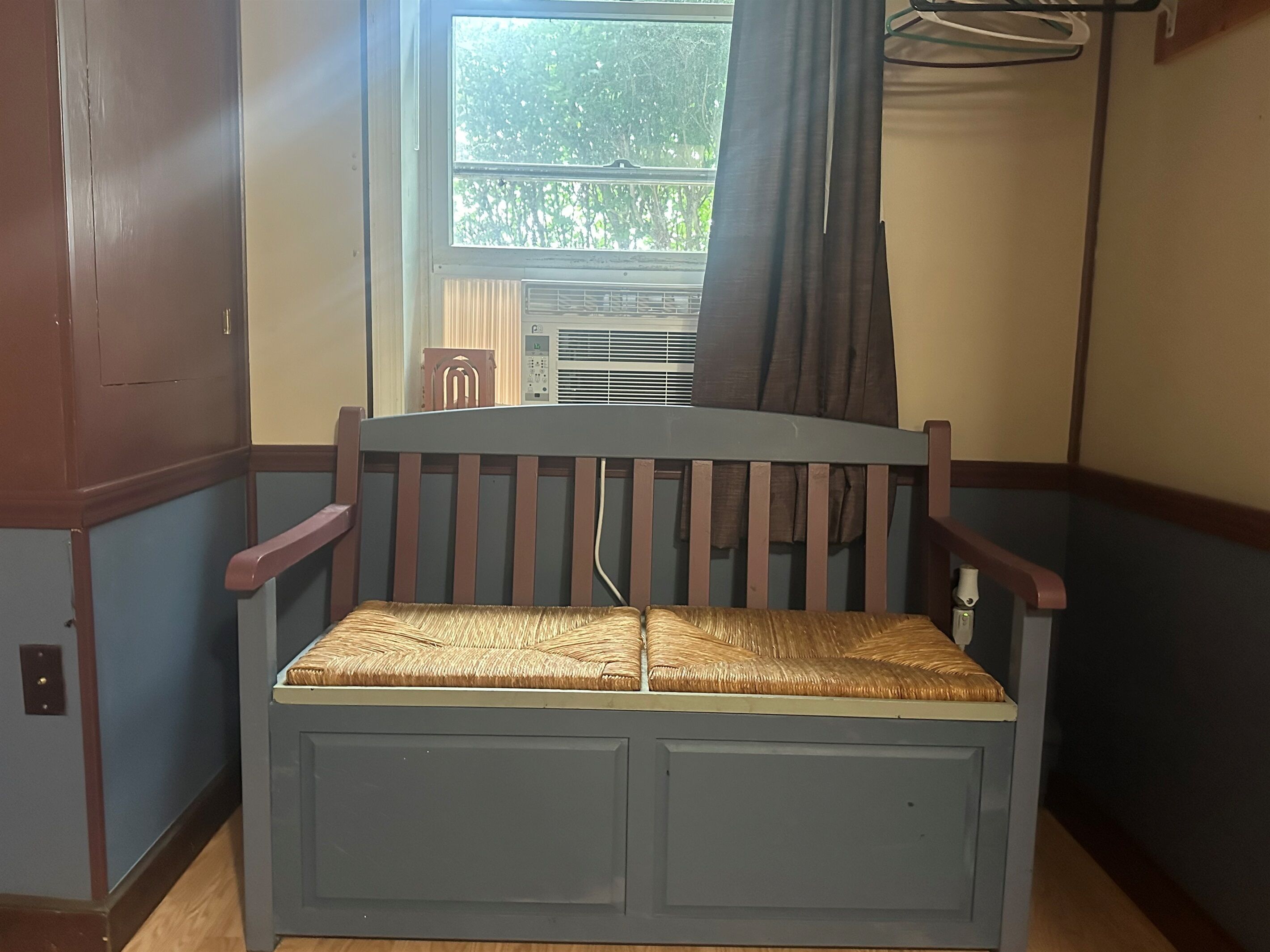 Ein Eckzimmer mit einer Holzbank, einem fenster mit Vorhängen und einer Heizung.