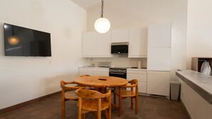 A compact kitchen with white cabinets, a stove, and a dining table with four chairs.