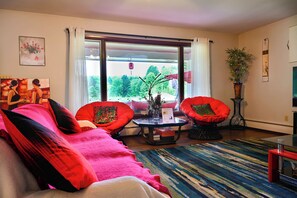 Ein Wohnzimmer mit einer Couch, zwei Sesseln, einem Couchtisch, einer Topfpflanze und Blick ins Freie.