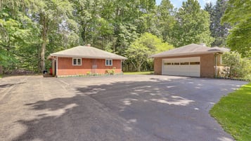 Une maison à deux étages avec un garage, entourée d’une allée et d’arbres.