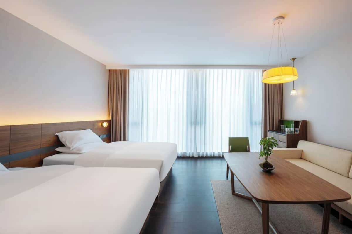 A hotel room with two beds, a sofa, a wooden table, and a TV.
