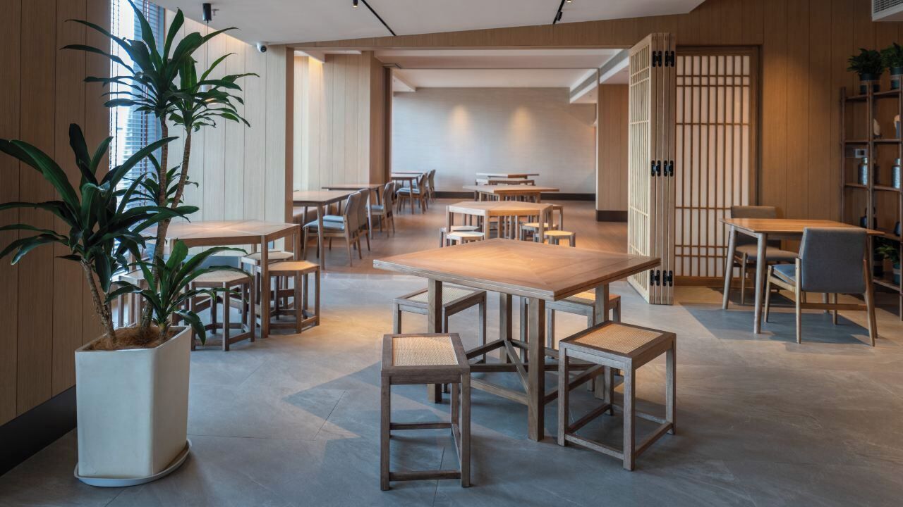 Ein modernes Interieur mit Holztischen und -stühlen, einer großen Pflanze im Topf und einem traditionellen japanischen Raumteiler.