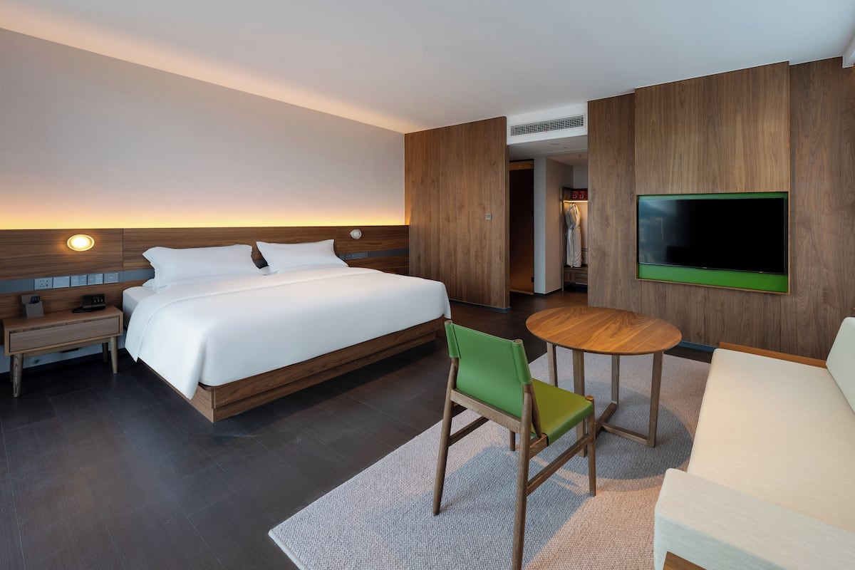 A hotel room with a large bed, a TV mounted on the wall, a small table, and a sofa.