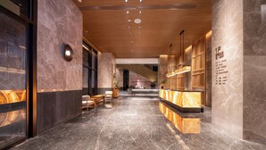 Un moderno vestíbulo de hotel con pisos de mármol, una recepción, zonas de estar y una escalera que conduce a los pisos superiores.