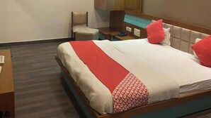 A hotel room with a bed, a desk, a chair, a wardrobe, and a ceiling fan. - Hotel Raghupati - Ayodhya (Faizabad)