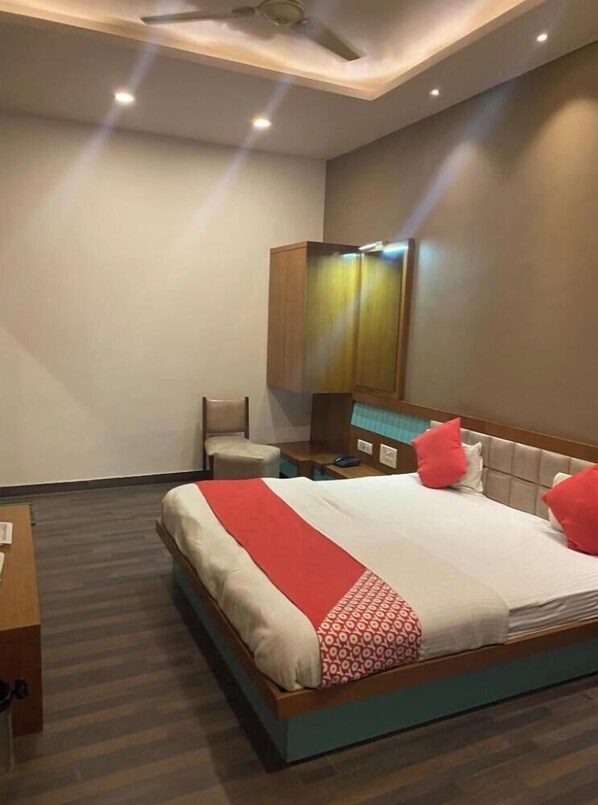 A hotel room with a bed, a desk, a chair, a wardrobe, and a ceiling fan. - Hotel Raghupati - Ayodhya (Faizabad)
