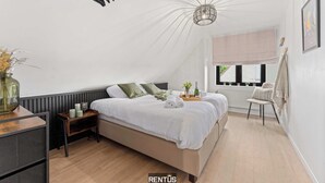 Une chambre avec un grand lit, une table de chevet, une chaise, une fenêtre donnant sur un beau paysage et un ventilateur de plafond.