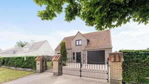 Une maison à deux étages avec un toit en tuiles, un garage et une allée menant à une porte grillagée.