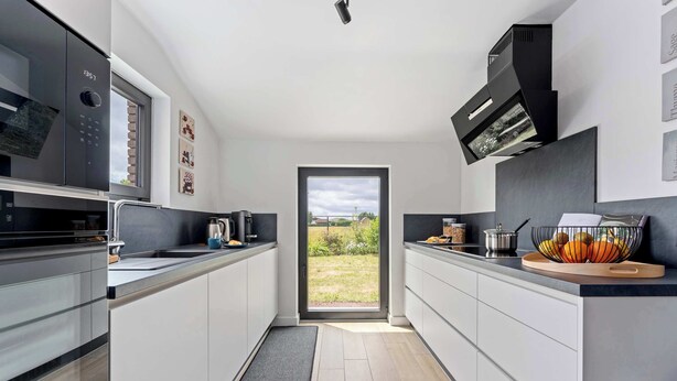 Une cuisine moderne avec des meubles blancs, une hotte noire et une fenêtre donnant sur un jardin.