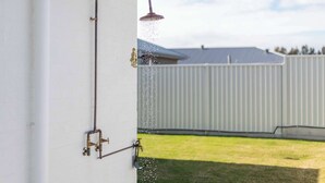 A water spout with a showerhead attached to a wall, with water spraying out. - Eden - Oceanstays - Pet friendly (Yamba)
