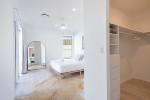 Un dormitorio con cama, espejo, ventana, armario y puerta que da a otra habitación.