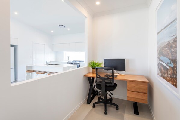 Una cocina moderna con una isla central, una zona de comedor con taburetes, un escritorio de madera con una computadora y un cuadro en la pared.