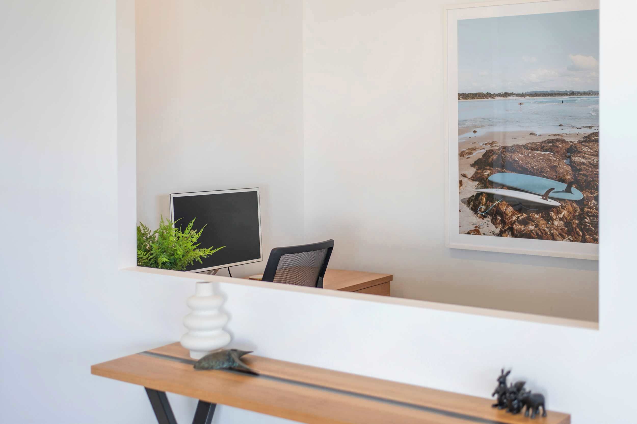 A room with a desk, chair, computer, and a framed picture of a beach scene.