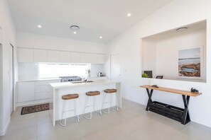 Una cocina moderna con armarios blancos, una isla central con taburetes, una barra de madera y un cuadro colgado en la pared.