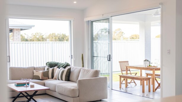 A modern living room with a sofa, a coffee table, and a dining area with a table and chairs. - Eden - Oceanstays - Pet friendly (Yamba)