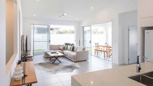 A modern kitchen with a built-in oven and a dining area with a table and chairs. - Eden - Oceanstays - Pet friendly (Yamba)