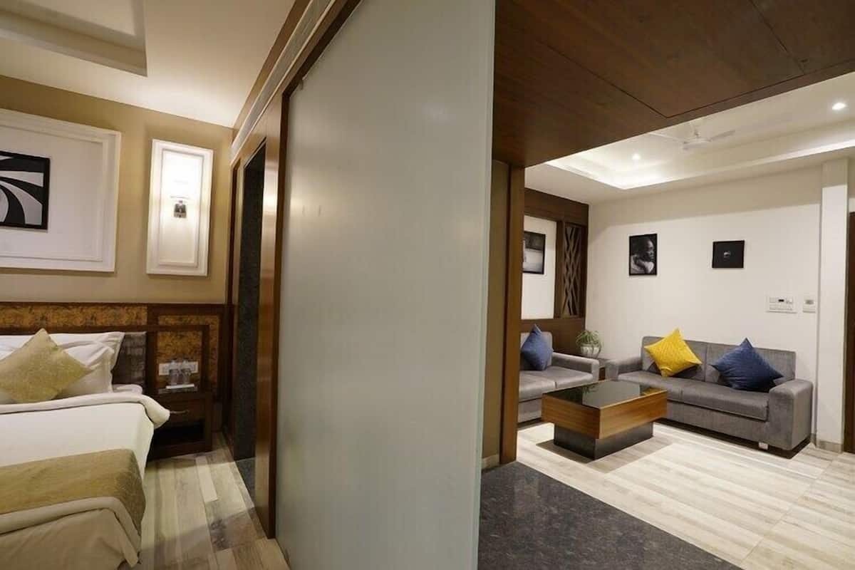 A modern hotel room with a bed, a seating area with a sofa and armchairs, and a coffee table.