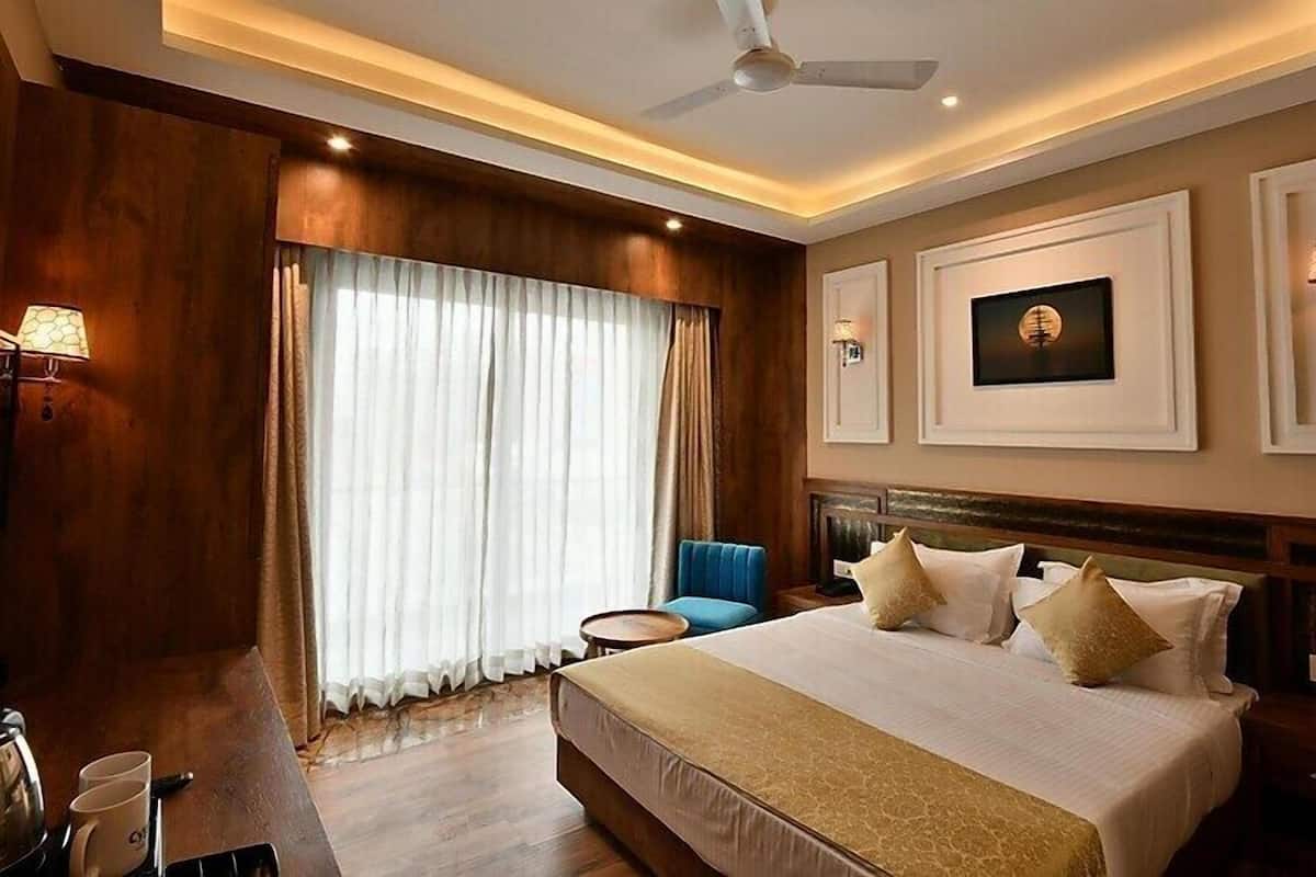 A hotel room with a large bed, a desk with a lamp, a chair, and a window with curtains.