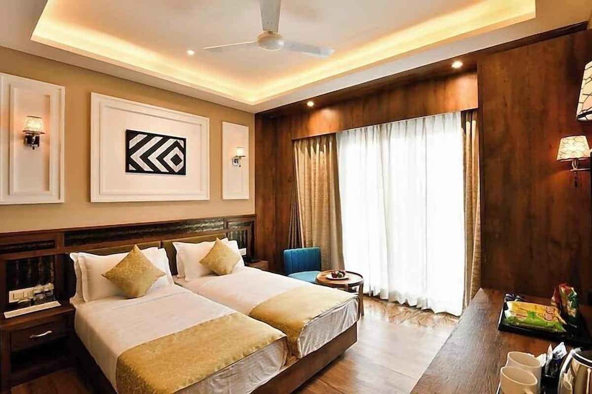 A hotel room with two beds, a ceiling fan, a large window with curtains, and a small table with a tray of snacks.