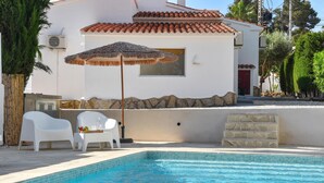 A swimming pool with a tiled edge, a white chair, a straw umbrella, and a stone wall. - Tres Corazones 6 pax - Moraira, Costa Blanca (Moraira)