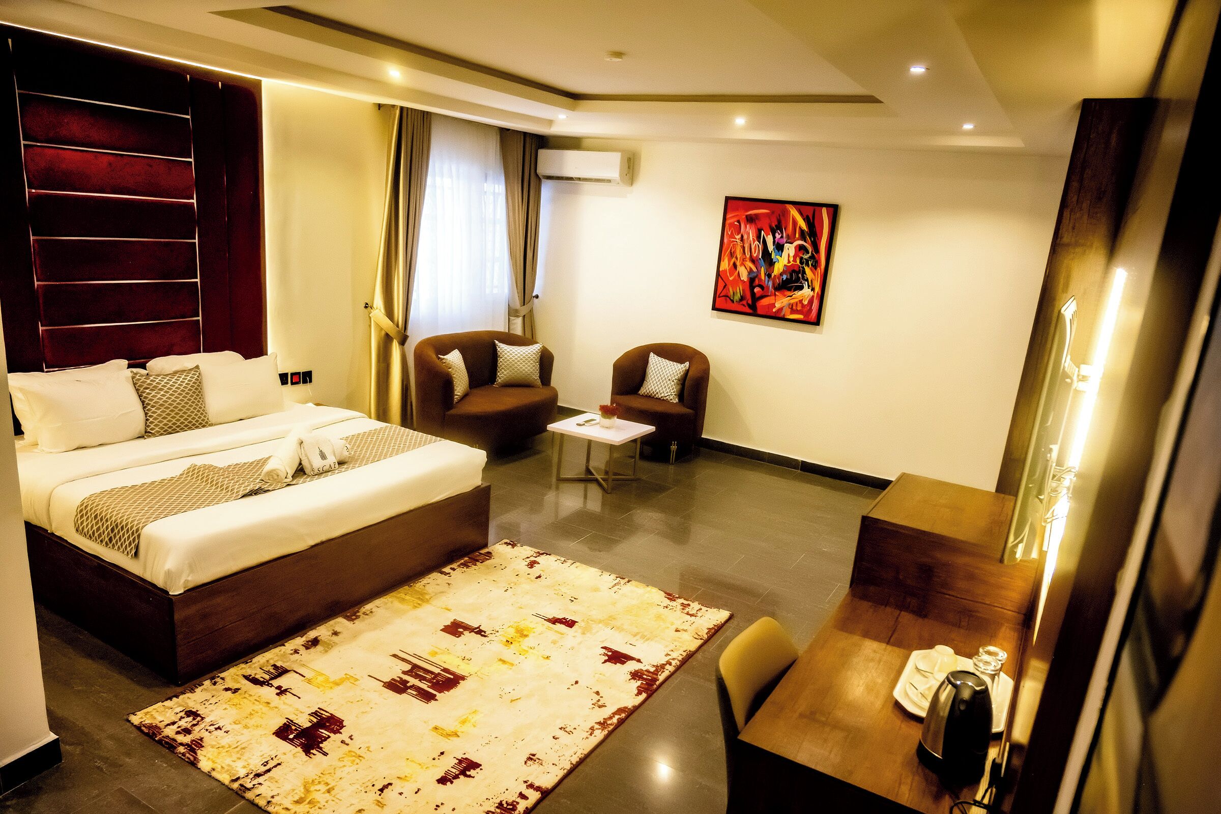 A hotel room with a large bed, two armchairs, a small table, and a desk with a chair.
