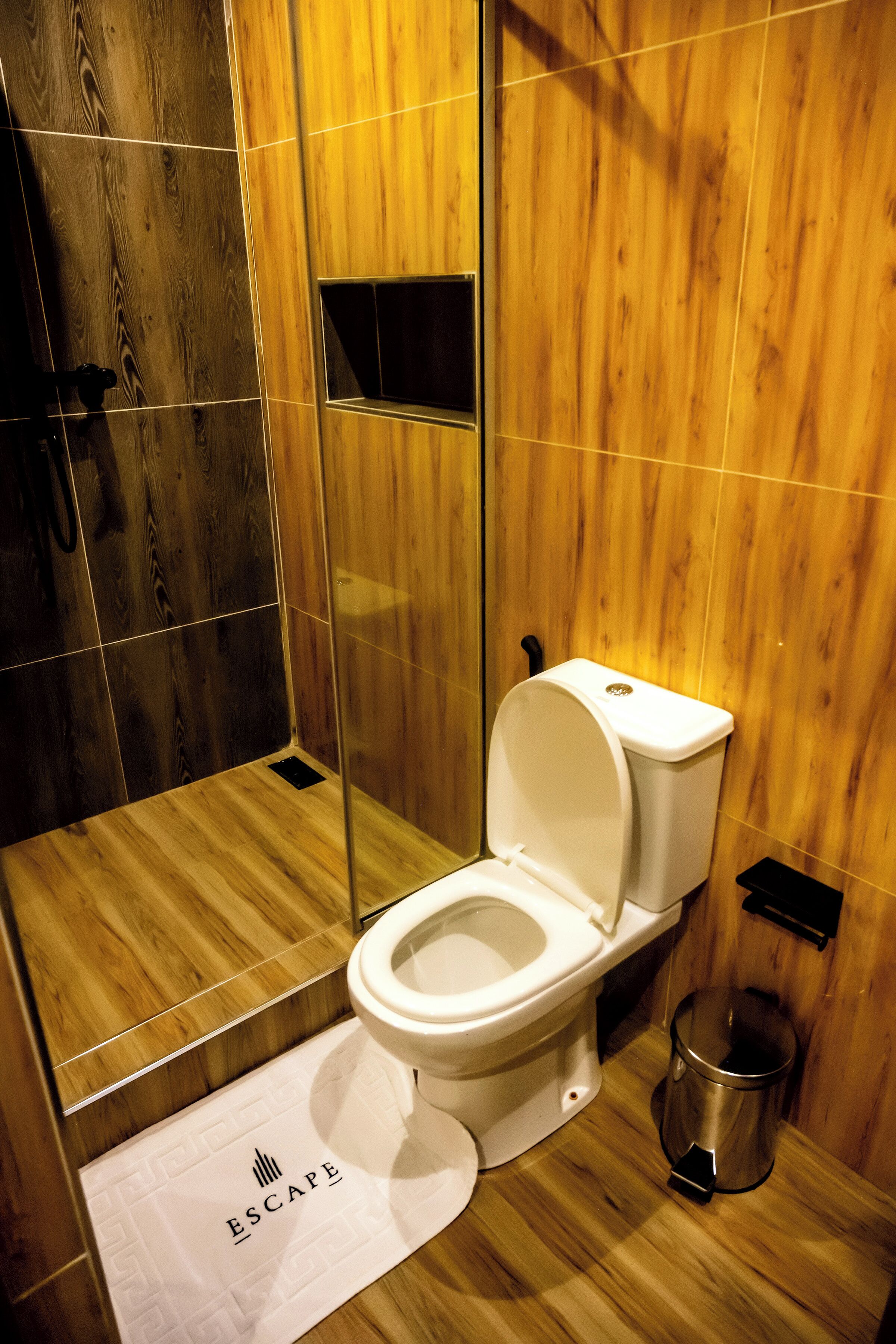 Een moderne badkamer met een wand van hout, een wit toilet en een douchegedeelte.