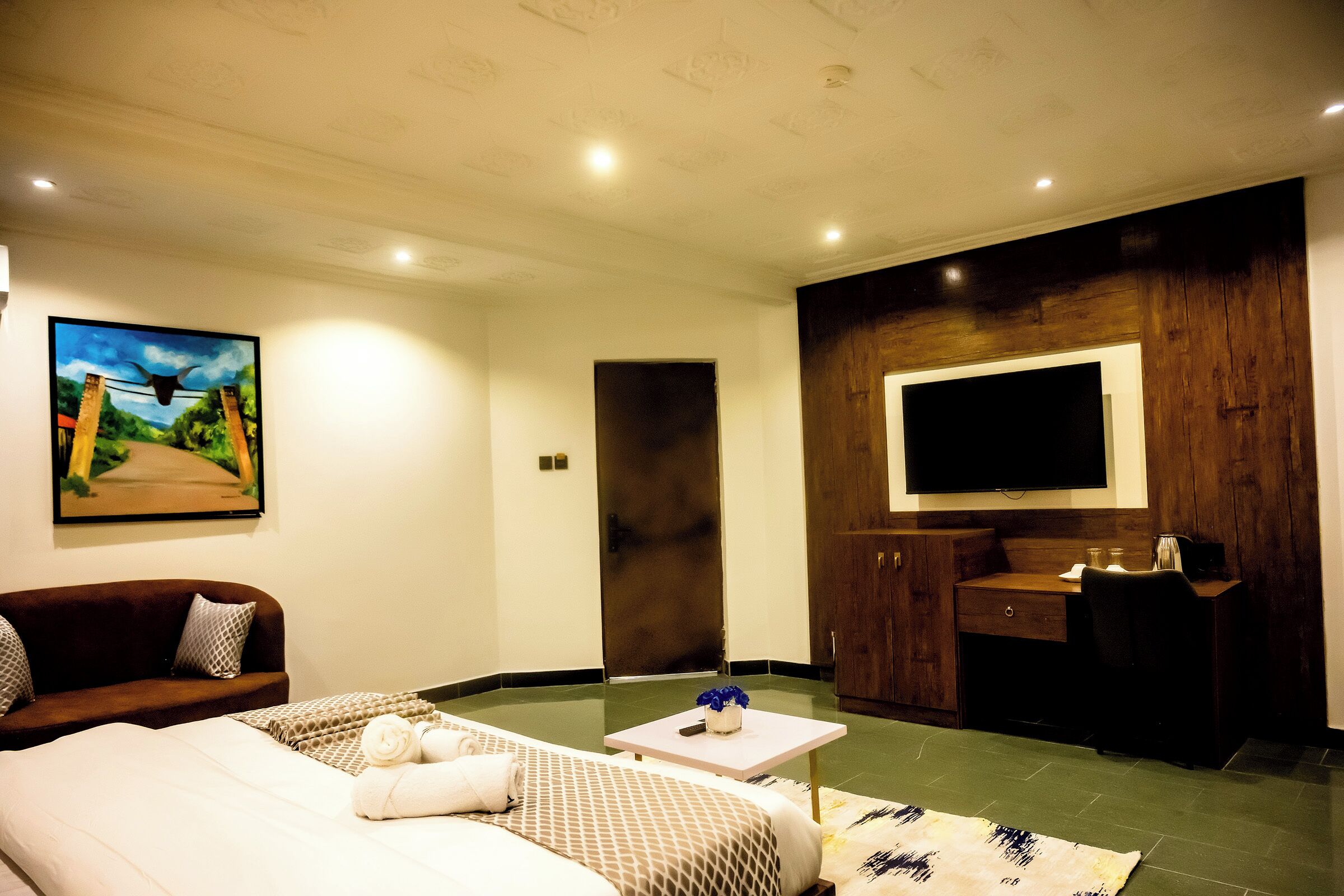 Ein Hotelzimmer mit Bett, Sofa, Schreibtisch, Fernseher und einem Gemälde an der Wand.