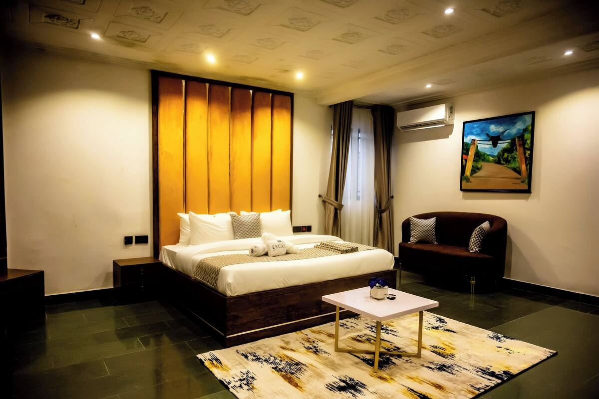 A modern hotel room with a large bed, a small table, a chair, and a painting on the wall.