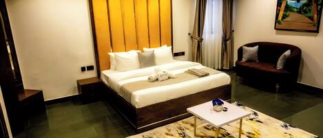 Une chambre d’hôtel moderne avec un grand lit, un petit canapé, une table basse et un tableau au mur.