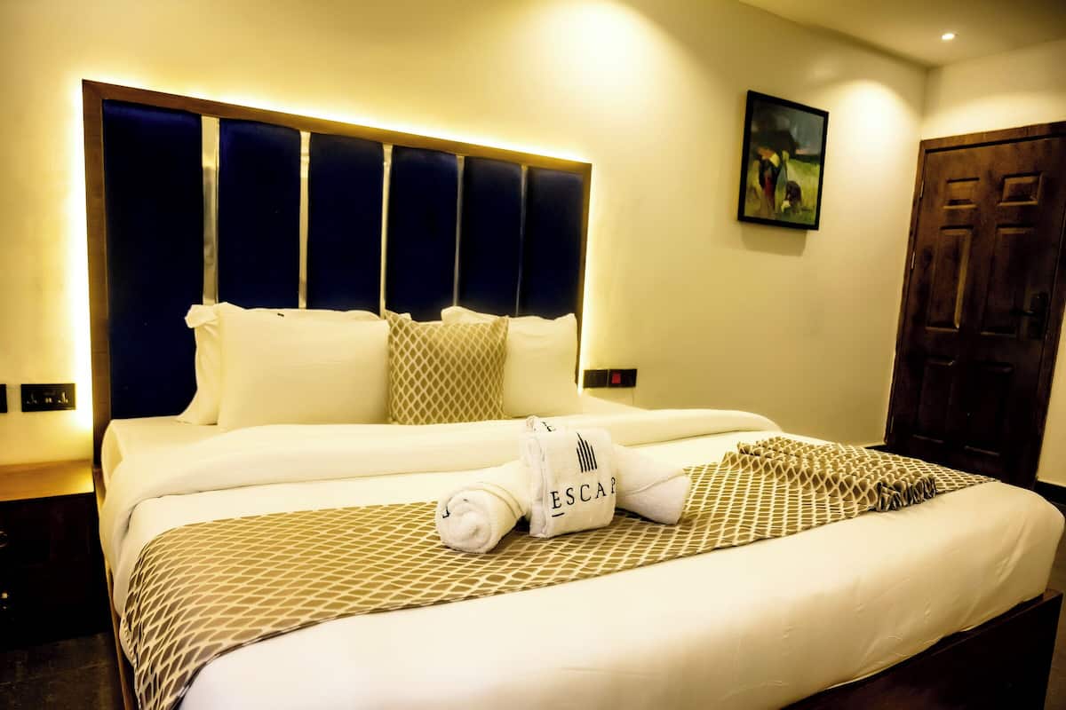 A hotel room with a large bed, a headboard with vertical panels, a wooden door, and a painting on the wall.