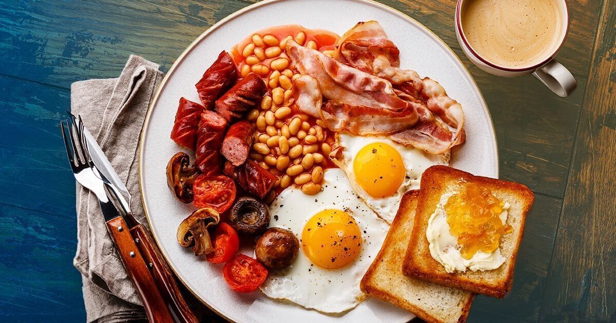 A plate of breakfast with eggs, bacon, sausages, beans, and toast.