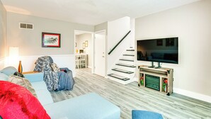 Una sala de estar con sofá, televisor montado en la pared, escalera y chimenea.