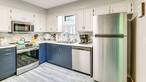 Una cocina moderna con armarios blancos, un refrigerador de acero inoxidable, un lavavajillas y un microondas.