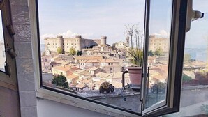 Habitación de esquina con un amplio ventanal con vistas a un casco antiguo, un sillón cómodo y un radiador abajo.