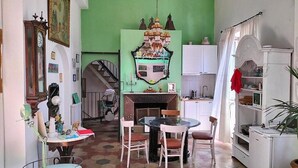 Una habitación con pared verde, chimenea, mesa de comedor con sillas, un reloj y una estantería.