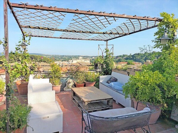 Terraza en la azotea con pérgola, zona de estar y plantas en macetas.