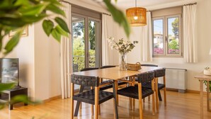 Un coin repas avec une table en bois, des chaises à revêtement noir, un luminaire suspendu et de grandes fenêtres avec des rideaux.