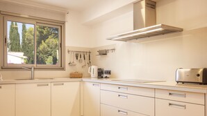 Une cuisine moderne avec des armoires blanches, une hotte de cuisinière en acier inoxydable et une fenêtre donnant sur les arbres.