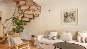 Un salon moderne avec un escalier en bois, un fauteuil en osier, un canapé agrémenté de coussins à rayures et un tableau encadré accroché au mur.