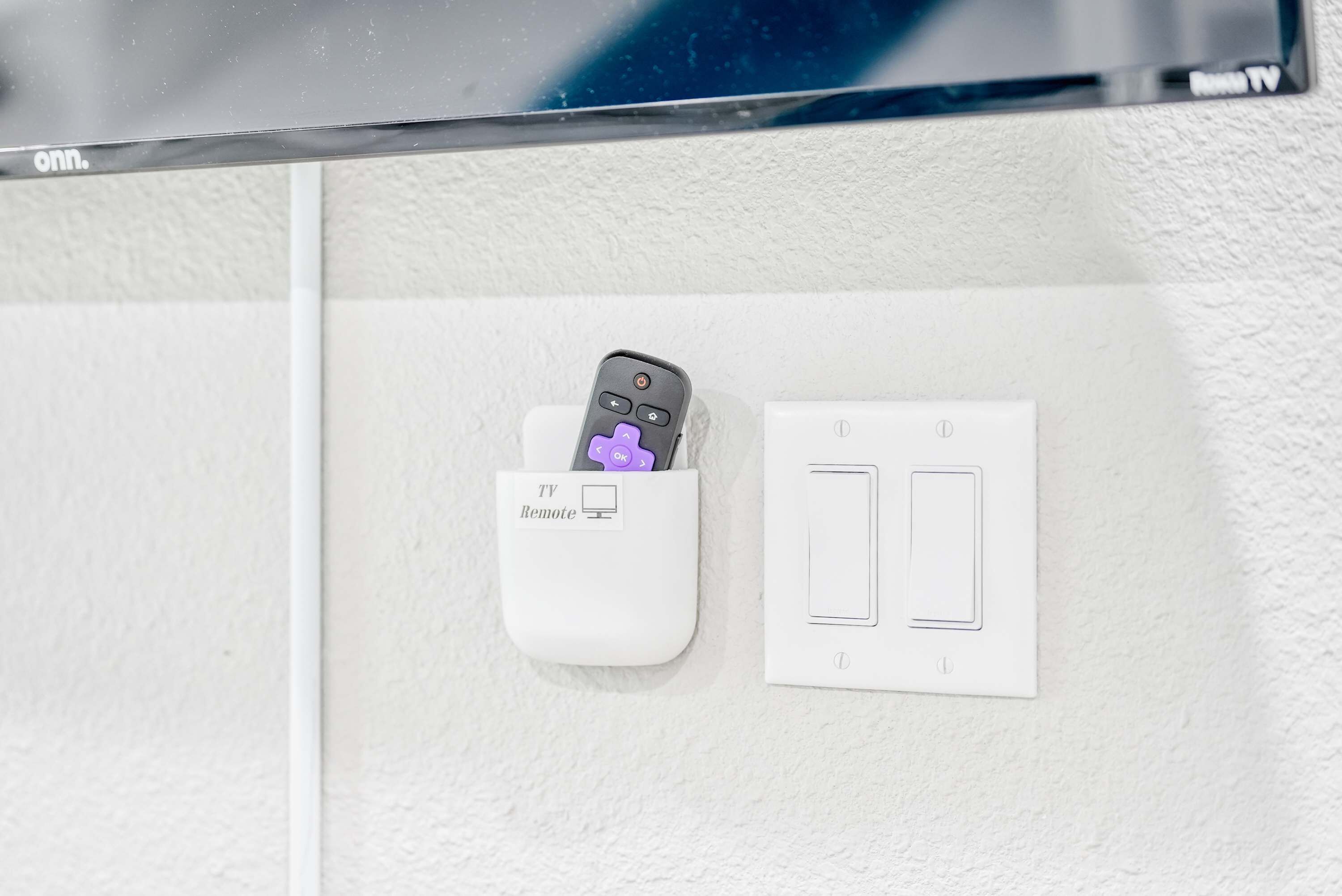 A TV remote and a power outlet on a white wall.
