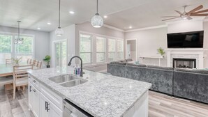A modern kitchen with a granite countertop, double sink, and a dining area with wooden furniture.
