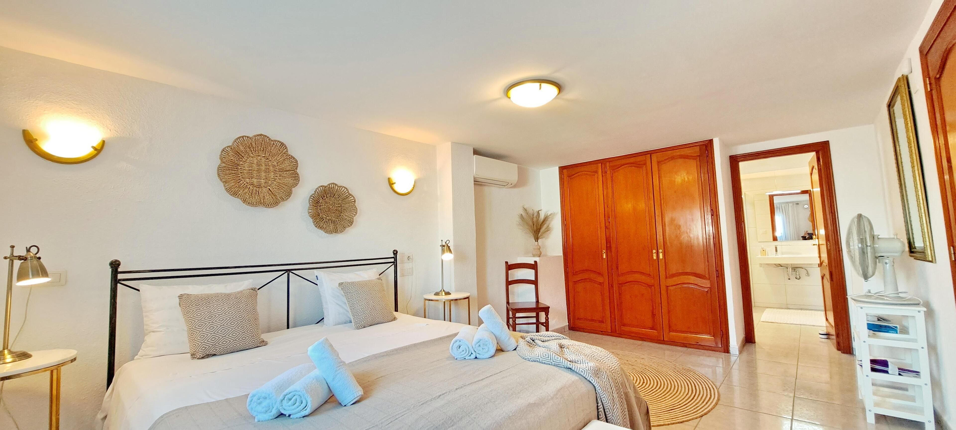 A neatly arranged bedroom with a bed, bedside lamps, decorative wall art, a wooden wardrobe, and a mirror.