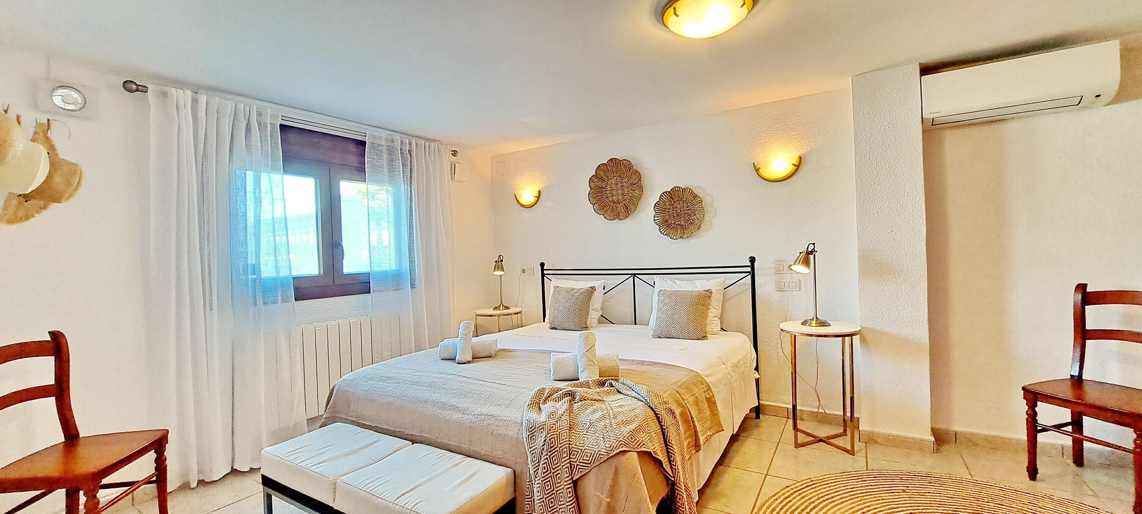 A bedroom with a bed, bedside tables, a window with curtains, a radiator, and wall-mounted lights.