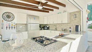 A modern kitchen with granite countertops, a built-in oven, and a stainless steel refrigerator. There is a clock on the wall and a ceiling fan above the kitchen. - Villa Esmeralda by Solidays - Moraira, Costa Blanca (Moraira)