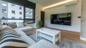 A modern living room with a large TV, a sofa, a coffee table, and a potted plant. - Diseño y confort en Via Cornelia (Santander)