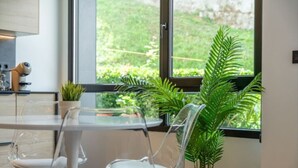 A modern kitchen with a glass table and chairs, a potted plant, and a view of greenery outside. - Diseño y confort en Via Cornelia (Santander)