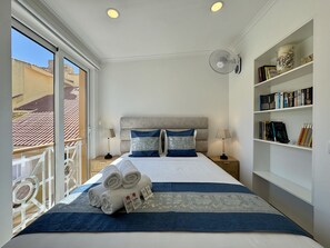 Ein Hotelzimmer mit einem Bett, zwei Nachttischen, einem Bücherregal und einem Balkon mit Geländer.