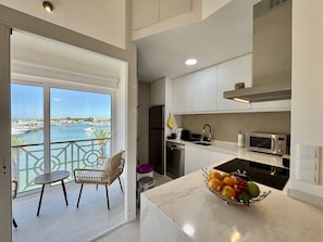 Una cocina moderna con vista al puerto deportivo, un comedor con mesa y sillas, y un frutero en la encimera.