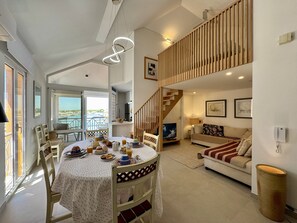 A spacious living area with a dining table set for a meal, a sofa, and a staircase leading to an upper level.