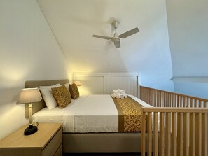 A hotel room with a bed, a nightstand, a lamp, a ceiling fan, and a wooden railing.
